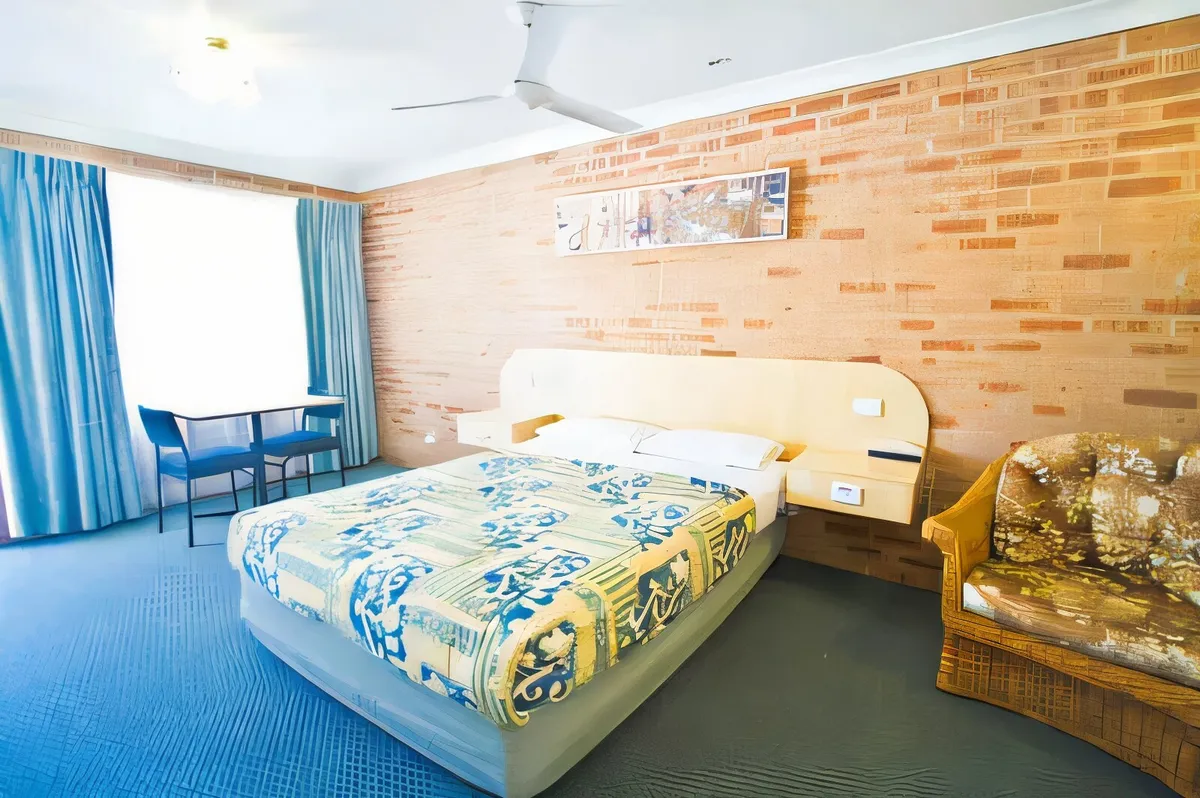Queen room with an exposed brick feature wall, armchair and table by the window