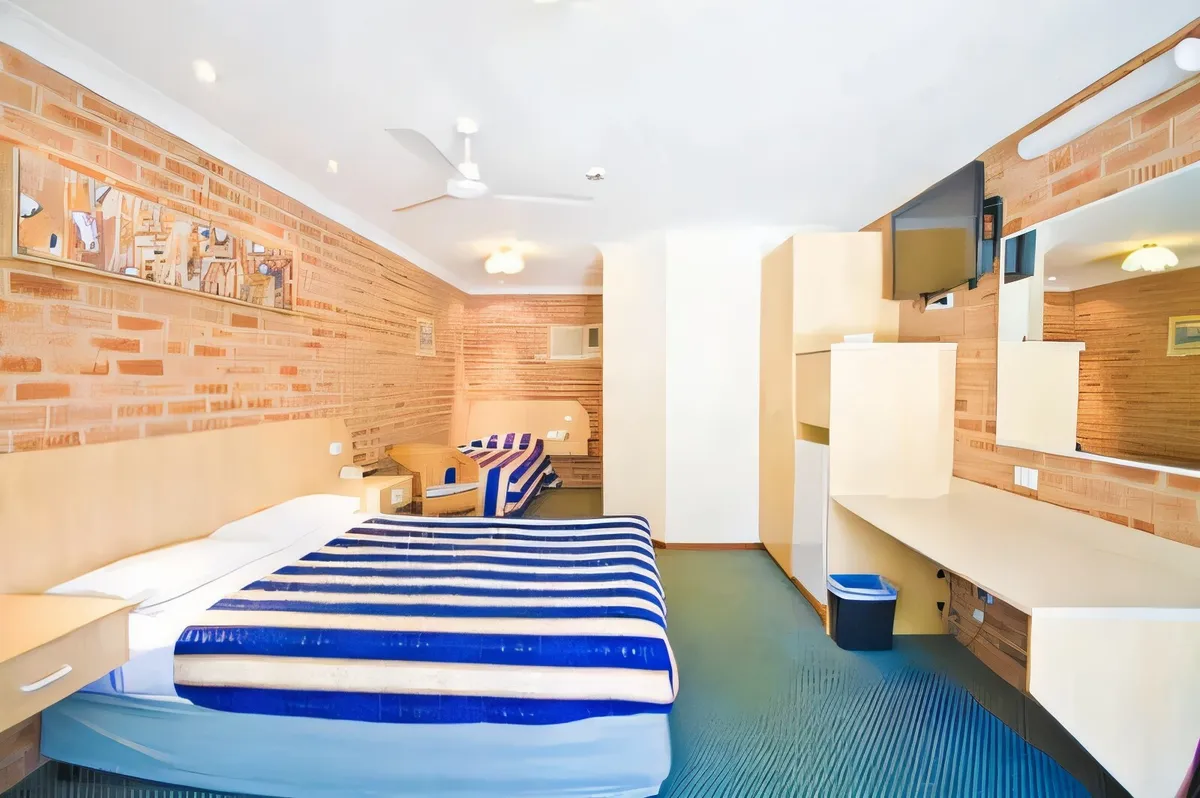 A family unit with queen and single beds, kitchenette bench and wall-mounted TV