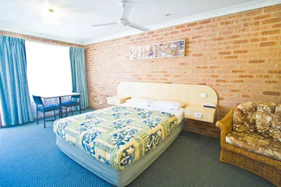 A motel room with a queen bed, exposed brick wall and blue curtains